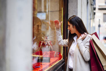 Young woman carrying bags while looking through store window - PGF00472