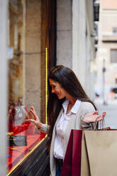 Smiling woman touching glass while window shopping - PGF00474