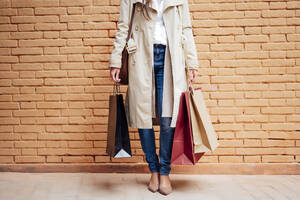 Woman with shopping bags in front of brick wall - PGF00483