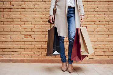 Woman holding shopping bags while standing in front of brick wall - PGF00484