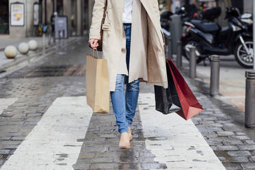 Woman with shopping bags walking on footpath while shopping in city - PGF00485