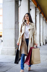 Lächelnde Frau auf dem Gehweg beim Einkaufen auf der Straße - PGF00486