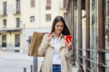 Junge Frau schaut beim Einkaufen in der Stadt auf ihr Smartphone - PGF00489