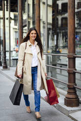 Young woman walking on footpath while shopping in city - PGF00494