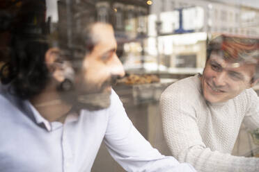 Männliche Mitarbeiter diskutieren in einem Coworking-Büro während einer Kaffeepause, gesehen durch Glas - FBAF01691