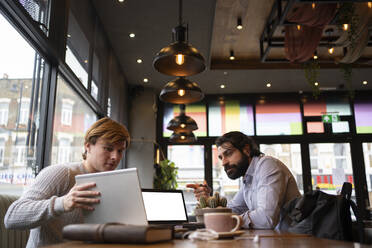 Geschäftsmann zeigt auf den Laptop, den ein Kollege in einem Coworking-Büro hält - FBAF01697