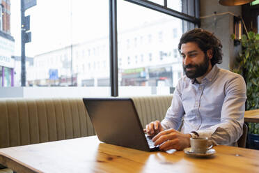 Gut aussehender Geschäftsmann, der einen Laptop benutzt, während er am Schreibtisch im Büro sitzt - FBAF01721