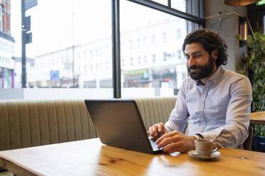 Handsome businessman using laptop while sitting at desk in office - FBAF01721