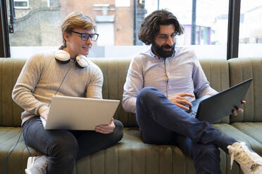 Männliche Unternehmer arbeiten am Laptop, während sie auf dem Sofa im Coworking-Büro sitzen - FBAF01725