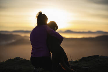 Junge Frau umarmt ihren Hund bei Sonnenaufgang - SNF01197