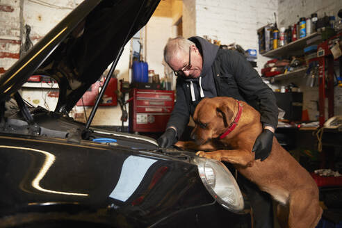 Männlicher Mechaniker repariert Auto, während er den Hund in der Garage betrachtet - PMF01743