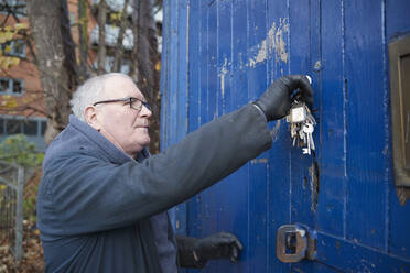 Kaukasischer männlicher Techniker mit Schlüssel, der die Tür einer Werkstatt öffnet - PMF01747