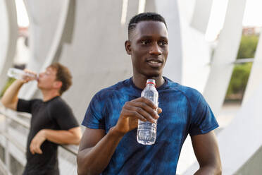 Männlicher Sportler schaut weg, während er eine Wasserflasche hält - IFRF00496