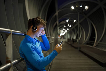 Young male athlete using mobile phone while leaning on footbridge railing - IFRF00507