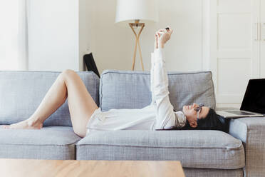 Female entrepreneur taking selfie while lying on sofa during working from home - MRRF00958