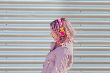Frau mit Kopfhörern, die an einer Wellblechwand steht, an einem sonnigen Tag - EIF00703