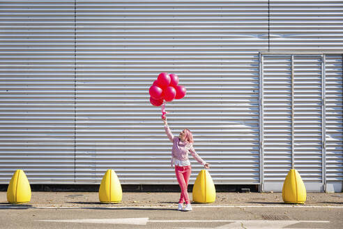 Frau in rosa Jacke betrachtet Luftballons auf der Straße - EIF00714