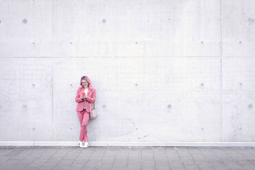 Frau in eleganter Freizeitkleidung, die vor einer Betonwand ein Mobiltelefon benutzt - EIF00733