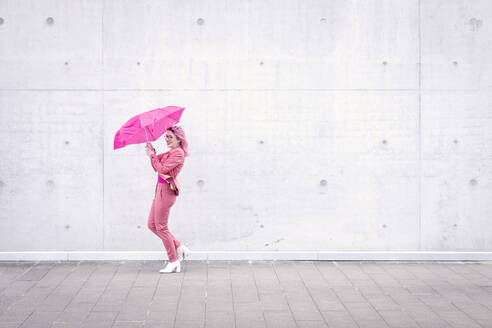 Happy woman holding pink umbrella on footpath - EIF00735