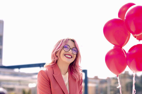 Happy woman looking away by pink balloons in front of sky - EIF00739