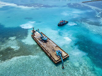 Luftaufnahme von Erdbewegungsmaschinen, die Masten auf einer schwimmenden Plattform im Male-Atoll transportieren - KNTF06190