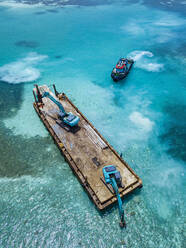 Luftaufnahme von Erdbewegungsmaschinen, die Masten auf einer schwimmenden Plattform im Male-Atoll transportieren - KNTF06191