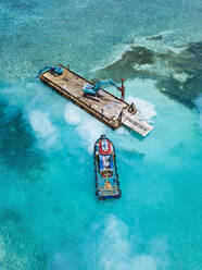 Luftaufnahme von Erdbewegungsmaschinen, die Masten auf einer schwimmenden Plattform im Male-Atoll transportieren - KNTF06193