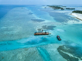 Luftaufnahme von Erdbewegungsmaschinen, die Masten auf einer schwimmenden Plattform im Male-Atoll transportieren - KNTF06195