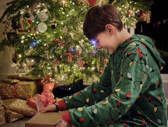 Smiling boy opening gift box by Christmas tree at home - PWF00267