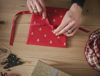 Woman tying red ribbon on gift over table during Christmas - PWF00271