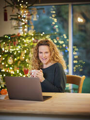 Lächelnde Frau, die einen Kaffee trinkt und auf einen Laptop schaut, während Weihnachten ist - PWF00276