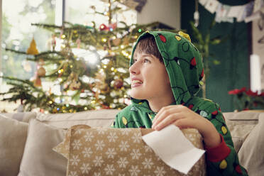 Smiling boy looking away while holding gift box during Christmas at home - PWF00286