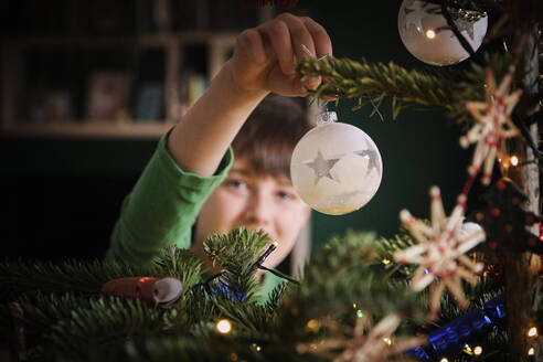 Junge schmückt Weihnachtsbaum mit Ornamenten zu Hause - PWF00296