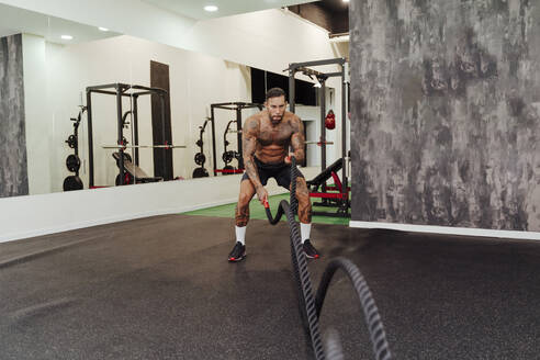 Männlicher Sportler, der in einem Fitnessstudio mit einem Seil trainiert - EBBF02833