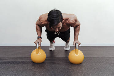 Männlicher Athlet macht Liegestütze auf einer gelben Kettlebell im Fitnessstudio - EBBF02840