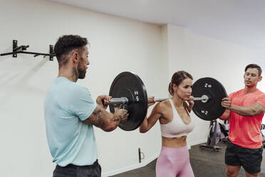 Athleten helfen einer Sportlerin beim Krafttraining mit einer Langhantel im Fitnessstudio - EBBF02848