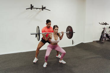 Fitnesstrainerin, die eine Sportlerin beim Training mit einer Hantel im Fitnessstudio anleitet - EBBF02852