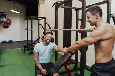 Männliche Freunde, die sich an den Geräten im Fitnessstudio die Hände reichen - EBBF02863