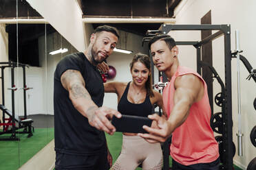 Sportliche Menschen, die ein Selfie mit ihrem Handy machen, während sie im Fitnessstudio stehen - EBBF02873