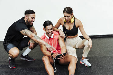 Sportler lachend bei der Benutzung eines Mobiltelefons durch Freunde im Fitnessstudio - EBBF02879