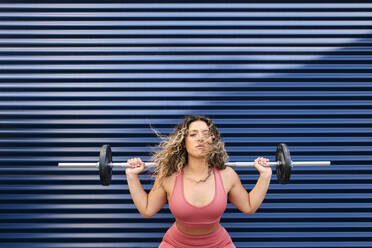 Sportswoman exercising with barbell in front of blue wall - AODF00392