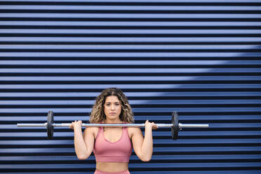 Female athlete lifting barbell while exercising in front of blue corrugated ball - AODF00402