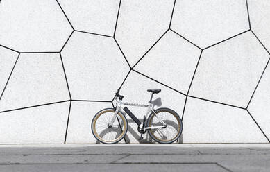 Fixie bicycle on footpath in front of white wall during sunny day - JAQF00438