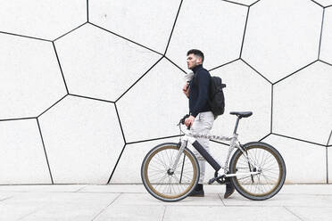 Junger Mann fährt mit dem Fahrrad an einer strukturierten weißen Wand vorbei - JAQF00439