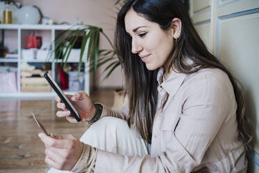 Mid adult woman using smart phone while holding credit card at home - EBBF02898