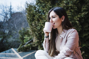 Woman drinking coffee while sitting on balcony - EBBF02900