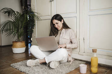 Female professional sitting cross-legged while using laptop at home - EBBF02902