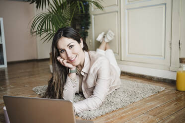 Beautiful woman in front of laptop lying on floor at home - EBBF02907