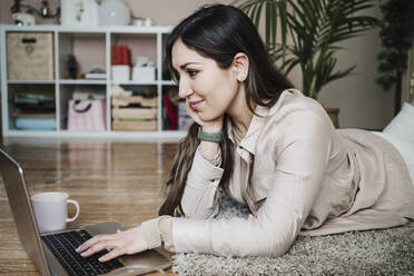 Weibliche Fachkraft liegt auf einem Teppich und benutzt einen Laptop zu Hause - EBBF02909