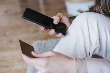 Hände einer Frau, die ein Smartphone benutzt, während sie zu Hause mit einer Kreditkarte bezahlt - EBBF02920